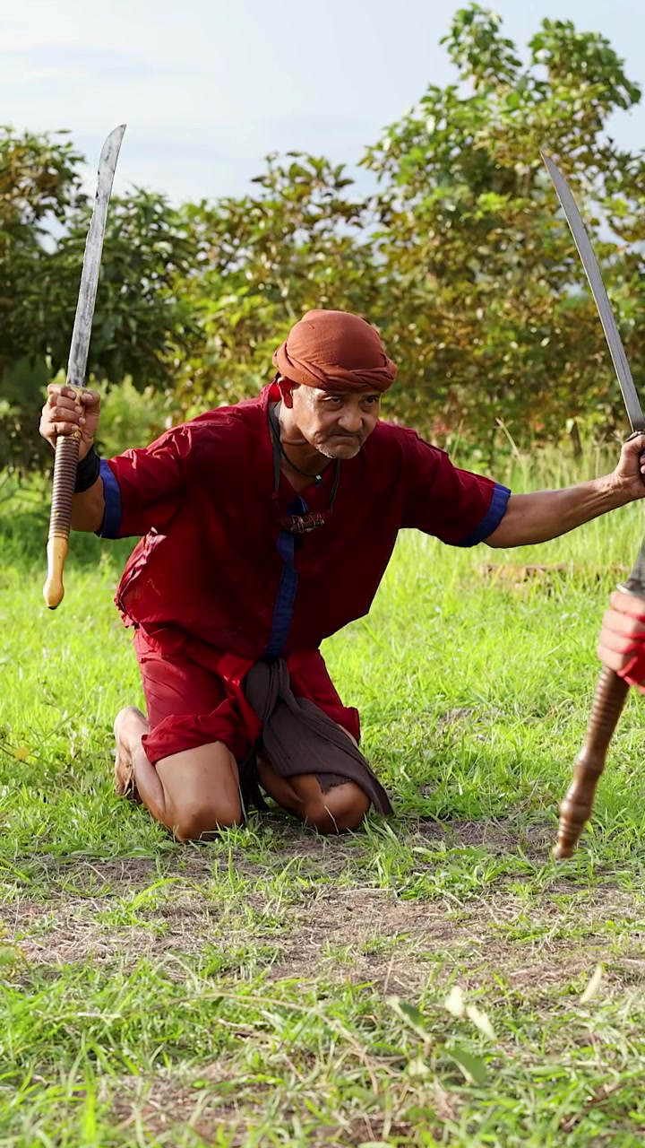 Un uomo in costume storico pratica tecniche di spada doppia su un campo erboso