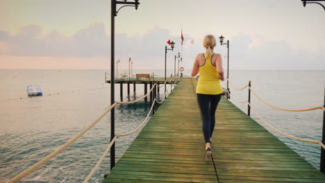 Aktiver-Lebensstil-Ein-Junges-Mädchen-In-Sportkleidung-Macht-Einen-Morgenlauf-Auf-Dem-Pier,-Um-Den-Sonnenaufgang-Zu-Treffen