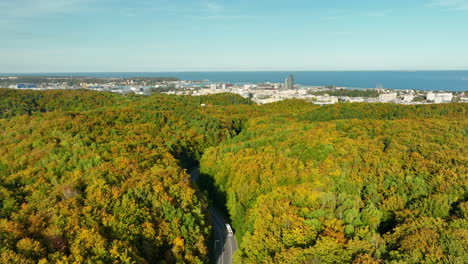 scenic aerial view of a winding forest road with a city skyline and sea in the background