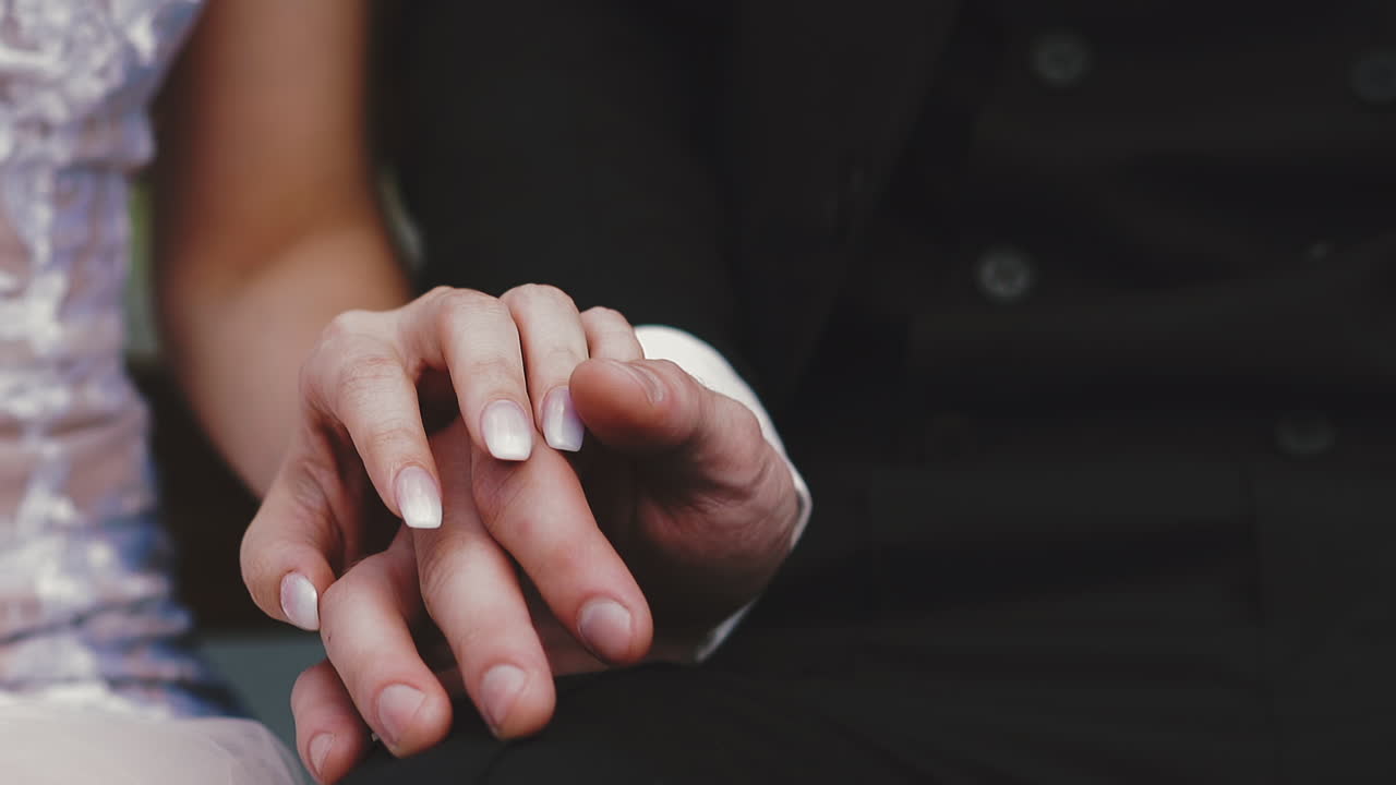 gentle lady in wedding dress joins hands with groom closeup