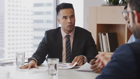 three businessmen sitting around table meeting in modern open plan office