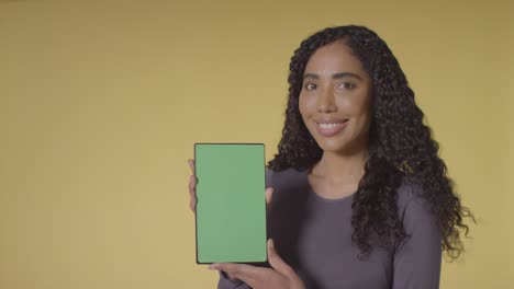 Studio-Portrait-Of-Smiling-Woman-Holding-Up-Digital-Tablet-With-Green-Screen