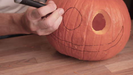 person carves eyes of a jack o' lantern on a pumpkin