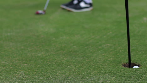 young boy golfing and putting golf ball into hole