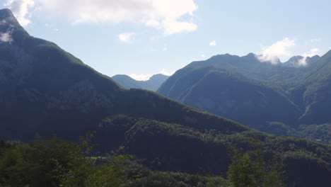 a panning shot of a green forested alpine mountain range