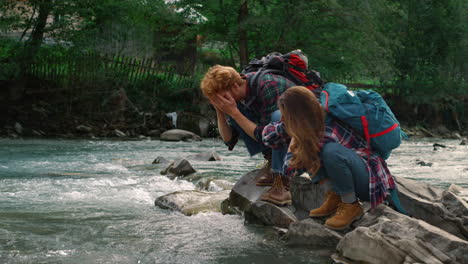 couple of tourists having rest at river. guy washing face with water from stream