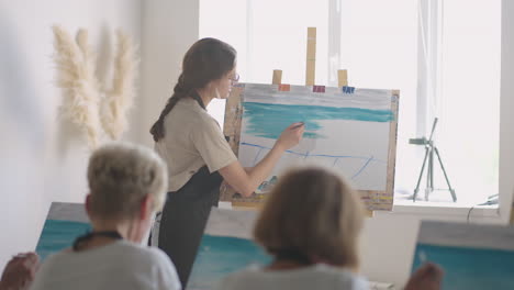 high angle view of cheerful senior friends painting on canvas. senior woman smiling while drawing with the group. seniors attending painting class together. senior men having fun painting in art class