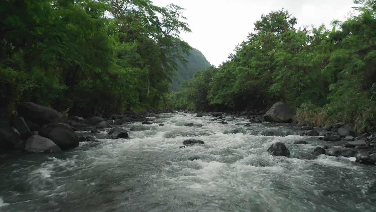 Donna in posizione del loto Sukhasana con le braccia alzate su una roccia accanto a un fiume tropicale, vista aerea