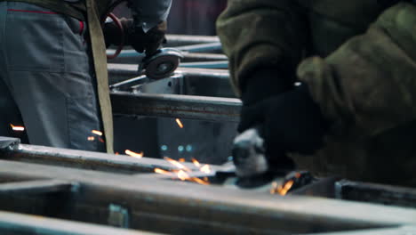 professional workers polishing metal surfaces with angle grinders in workshop