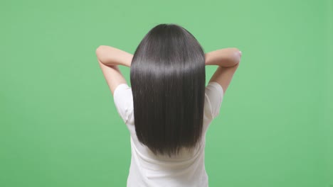 back view of a woman fluttering her long black and blond straight healthy hair in the green screen background studio