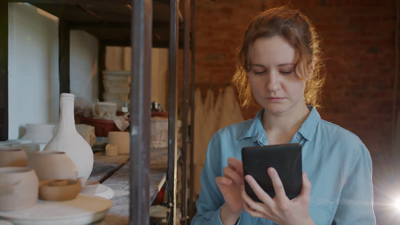 Woman working on a tablet in a pottery studio