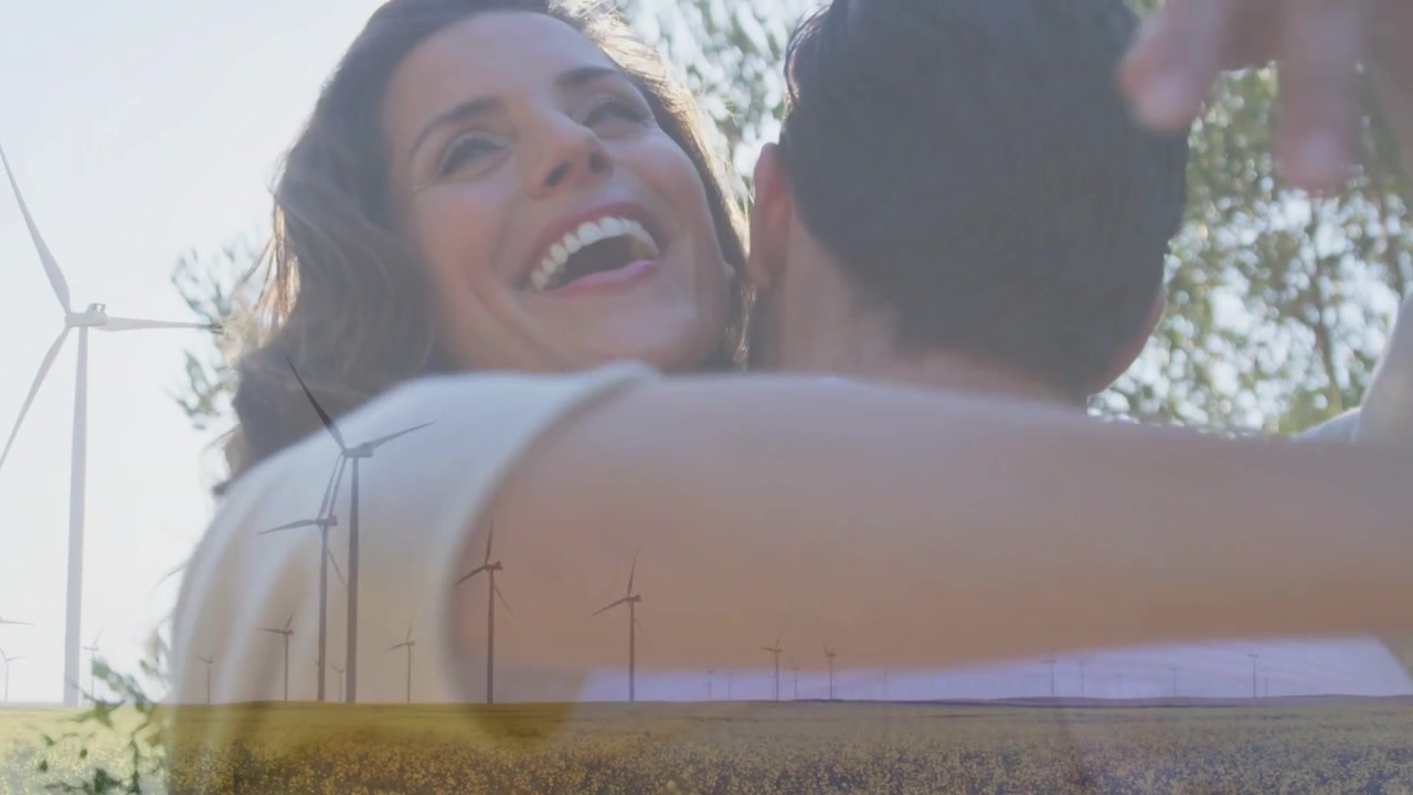 Mulher se aproximando, abraçando homem, sorrindo em campo ensolarado com turbinas, câmera se movendo para anúncios