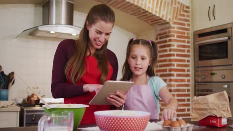 Madre-E-Hija-Caucásicas-Usando-Delantales-Usando-Una-Tableta-Digital-Mientras-Hornean-En-La-Cocina-De-Hom