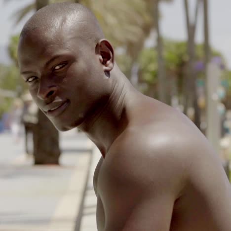 hombre negro musculoso sin camisa cerca de la playa de arena