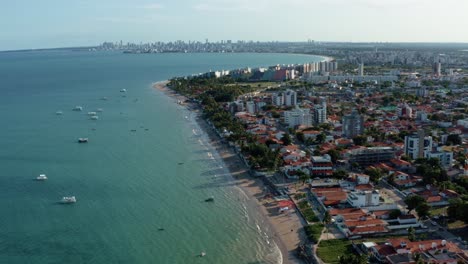 incline hacia arriba un dron aéreo tiro extremadamente ancho de la playa tropical de bessa en la ciudad de joao pessoa, paraiba, brasil con gente disfrutando del océano, botes turísticos y un gran paisaje urbano en el fondo