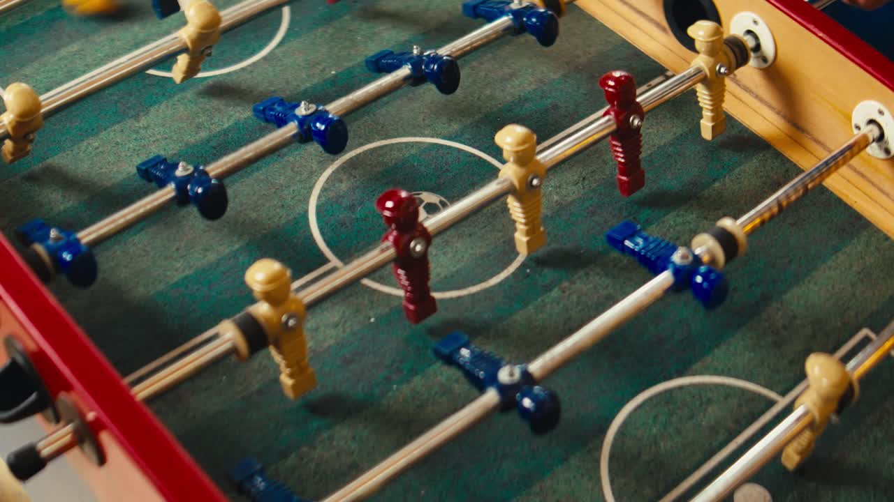 primer plano de un juego de mesa de futbolín con jugadores rojos y azules y una pelota blanca en movimiento