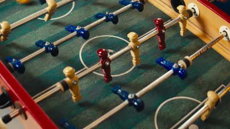 primer plano de un juego de mesa de futbolín con jugadores rojos y azules y una pelota blanca en movimiento