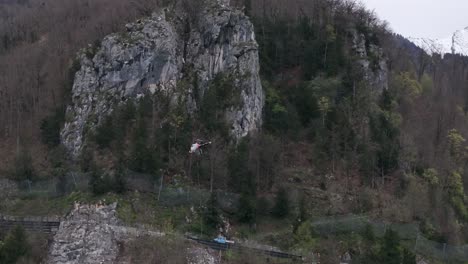 Ein-Hubschrauber-Fliegt-über-Ein-Tal-Und-Transportiert-Ein-Objekt-Mit-Einem-Seil---Es-Ist-Winter-Und-Auf-Den-Bergen-Liegt-Schnee