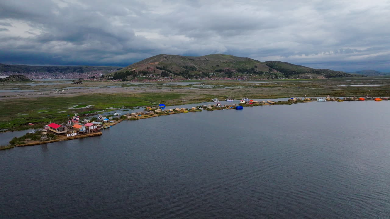 Aerial drone view of the Uros floating islands on Lake Titicaca near Puno, Peru. The man-made reed islands are dotted with traditional houses and boats, with mountains in the background