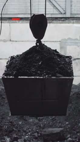bucket with charcoal hangs on crane hoist over pool at power generating station. rock fuel storage at water heating station. fossil sources usage