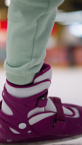 primer plano de una mujer cayendo mientras patina en una pista de hielo, con patines púrpuras y pantalones verdes menta