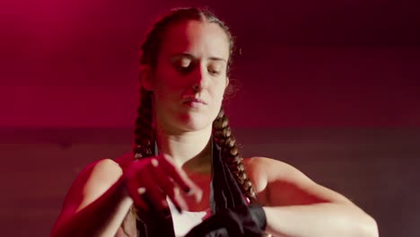 young caucasian sportswoman with braided pigtails wrapping hands with boxing bandages at gym