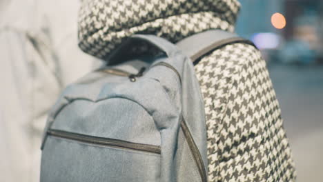 close-up of child wearing houndstooth jacket with light blue backpack, walking outdoors on urban street, showcasing school routine, outerwear fashion, and daily commute in soft evening city light