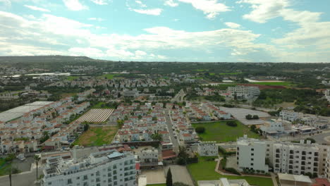 Perspectiva-Aérea-Que-Muestra-Una-Vista-Amplia-De-Protaras,-Chipre,-Con-Hileras-De-Alojamientos-Residenciales-Y-Vacacionales,-Campos-Verdes-Y-Colinas-Distantes,-Lo-Que-Refleja-Un-Paisaje-Rural-Expansivo-Y-Desarrollado.