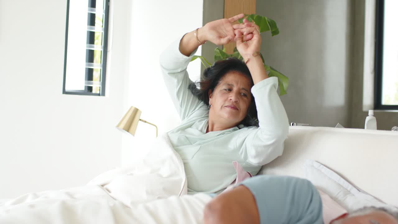 Coppia anziana, donna con un top color menta che si sveglia al sole, si avvicina al letto, accarezzando il partner che dorme per confortarlo.