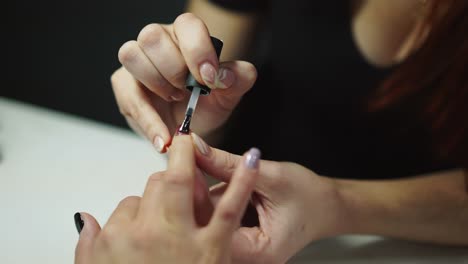 professional nail artist applies finish layer of clear nail polish on woman's nails with manicure in salon. master does manicure procedure to a female in the beauty center. close-up