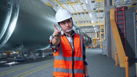 ingeniero asiático con casco de seguridad desaprueba sin señal del dedo índice mientras está de pie en una fábrica de tubos