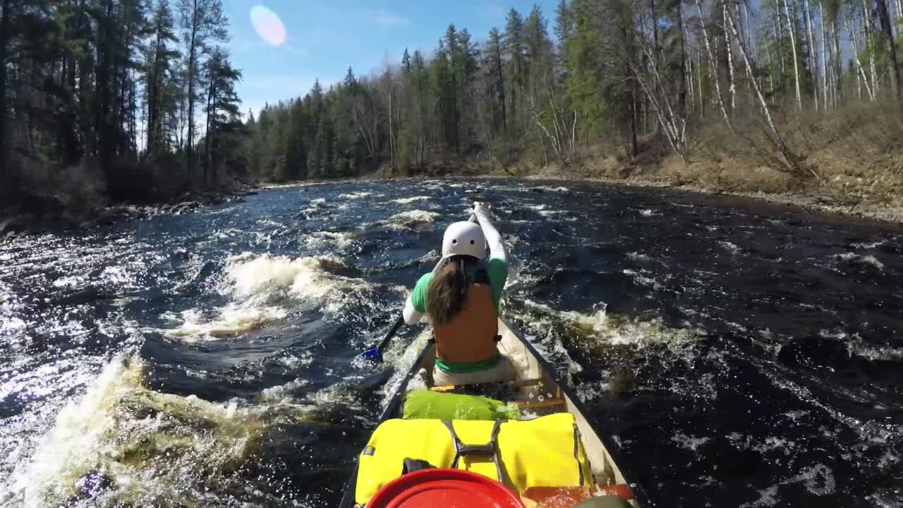 Ampia visuale di canoa su rapide selvagge di acque bianche su un fiume con una canoista che si inzuppa, Movimento lento