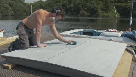 young shirtless man wiping down plywood engine cover with acetone before painting