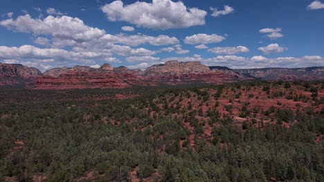 Aerial-drone-flying-outside-Sedona,-Arizona-from-Dry-Creek-Vista-over-a-valley-of-trees-towards-red-sandstone-rock-formations