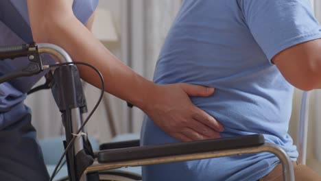 close up of male nurse helping patient who in a wheelchair to stand up by a walker during a physical therapy at home