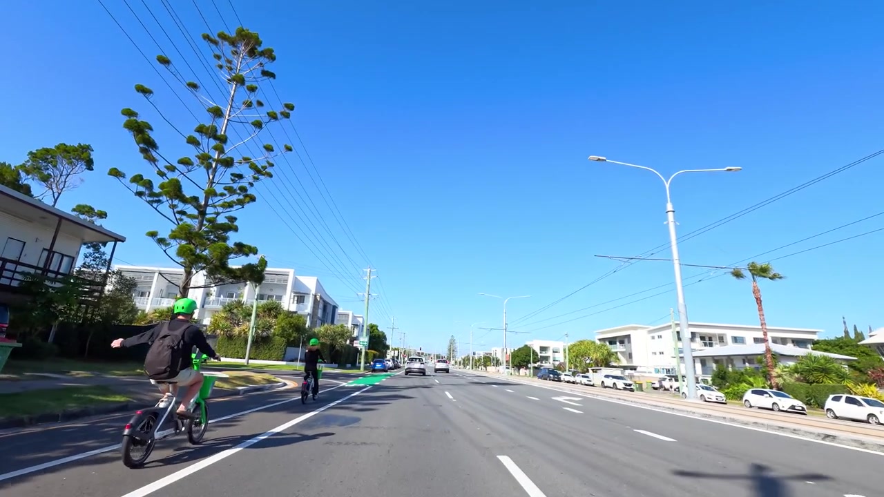 Lái xe dọc theo con đường ngoại ô đầy nắng với tàu điện nhẹ và người đi xe đạp.