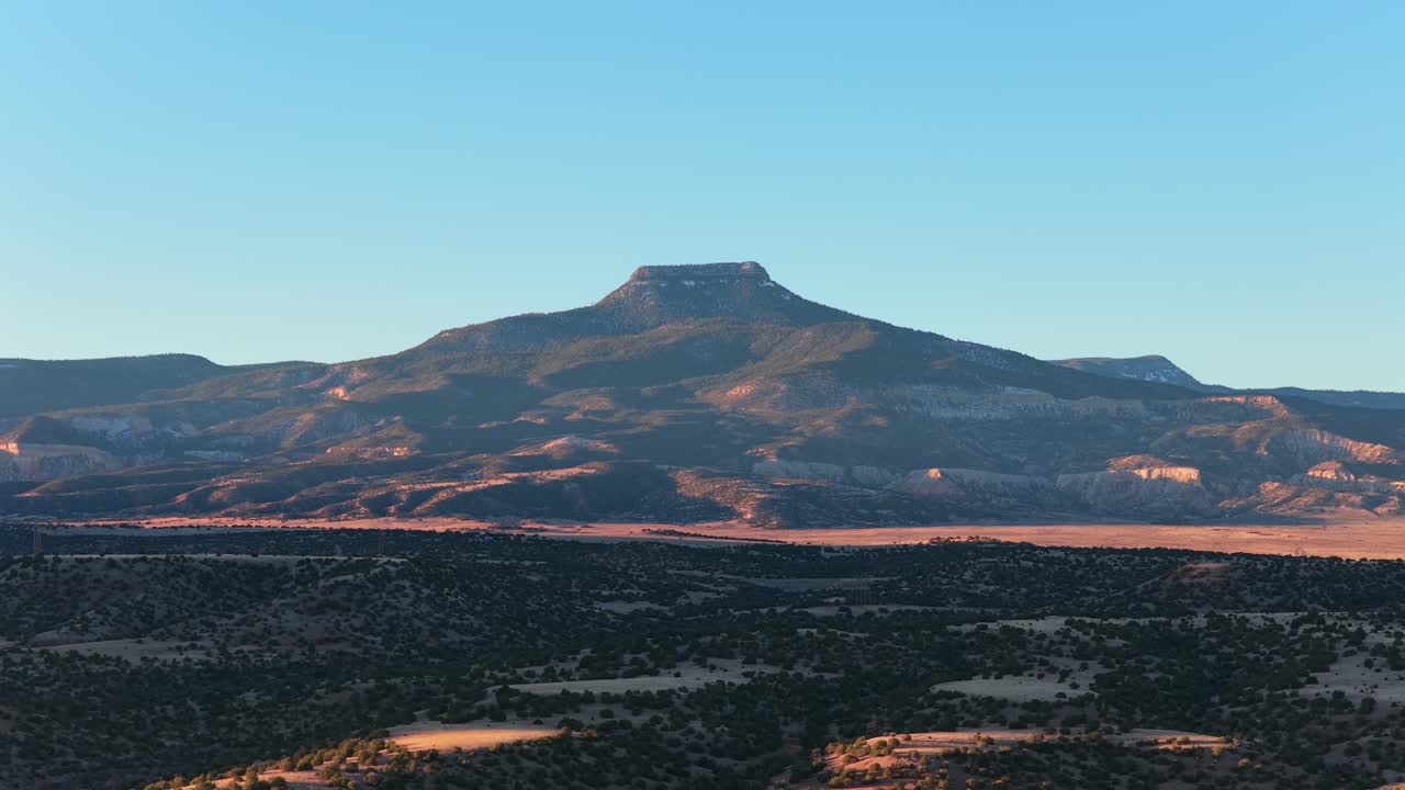 A cinematic drone approach moves closer to a flat-top mountain over a blue lake. Warm sunrise light hits the rugged desert landscape in this high-quality travel background