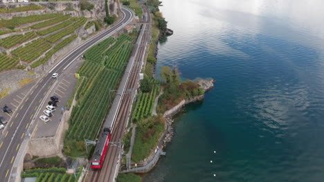 aerial of train driving through swiss countryside, tilting up and revealing beautiful lake with distant mountains