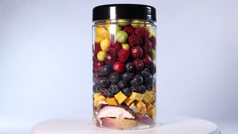 a transparent jar filled with a colorful assortment of freeze-dried fruits and vegetables, including blueberries, cranberries, raspberries, apple slices, pumpkin cubes, and more.
