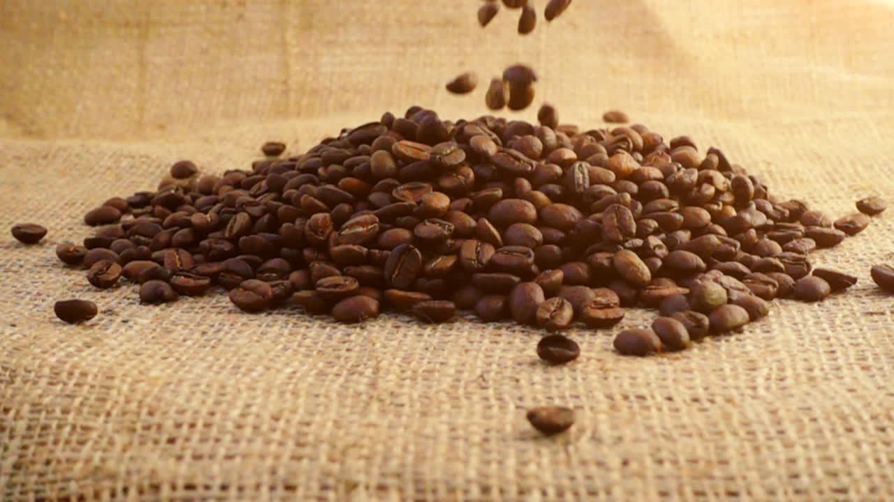 Chicchi di caffè cadono su tela di iuta al rallentatore.