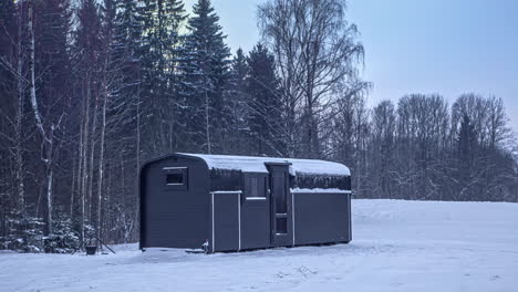 black cabin in snowy forest at sunset