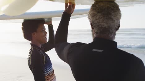 happy african american couple walking with surfboards on sunny beach