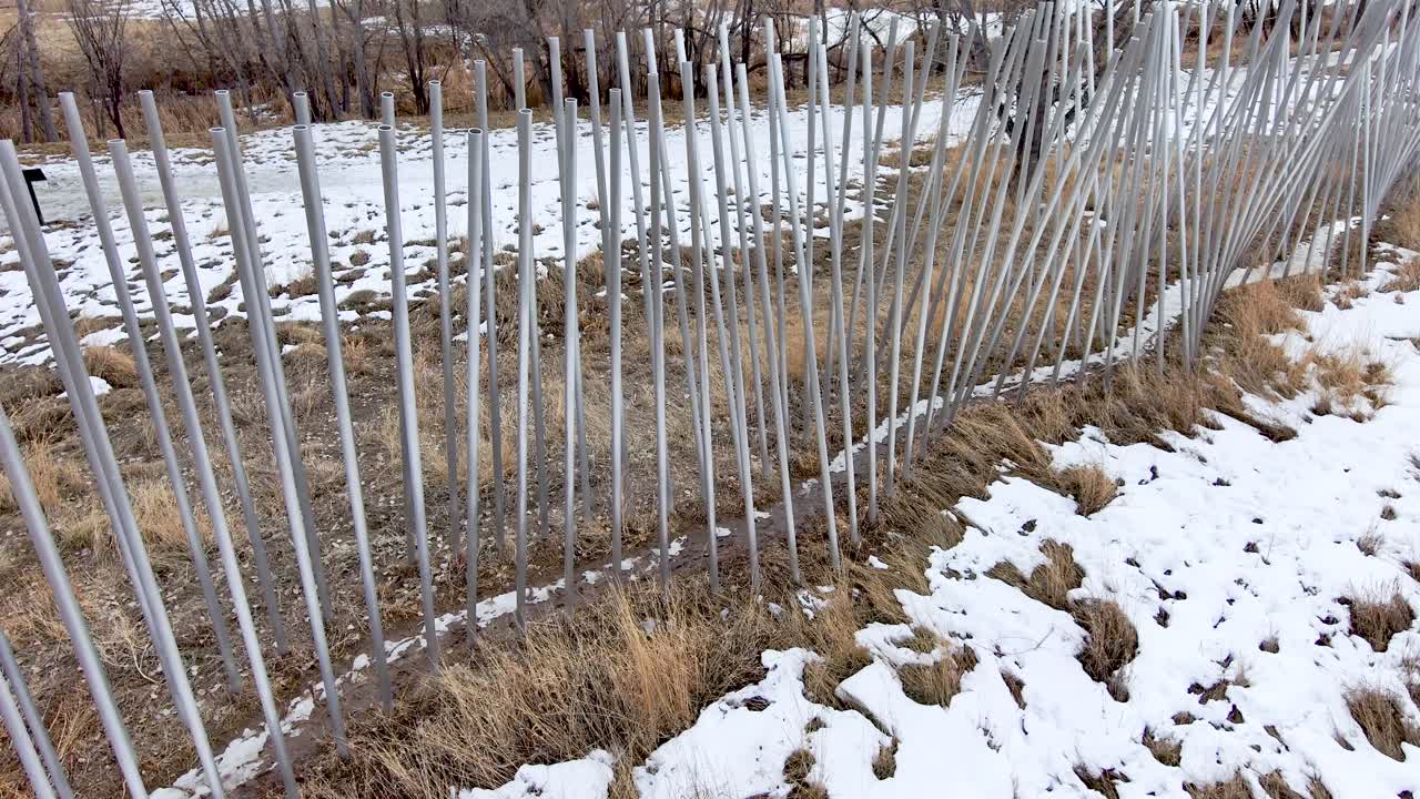 Aluminum tubes wind along a trail in rows like prison bars.