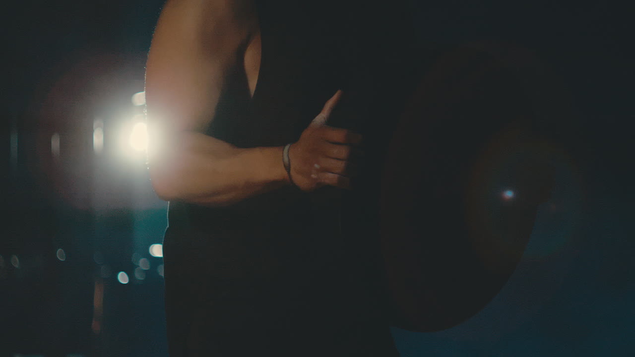 어두운 체육관에서 45 파운드의 접시와 함께 4k 800fps로 백라이트를하는 남성의 근접