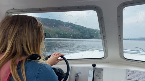 mujer con cabello rubio conduciendo un pequeño barco de motor blanco en un lago