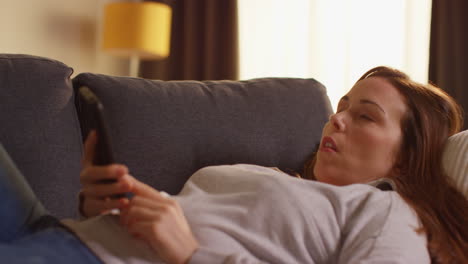 Woman-Lying-On-Sofa-At-Home-Fed-Up-And-Bored-With-Time-Wasted-Using-Mobile-Phone-To-Check-Social-Media-Message-And-Scroll-Online-1