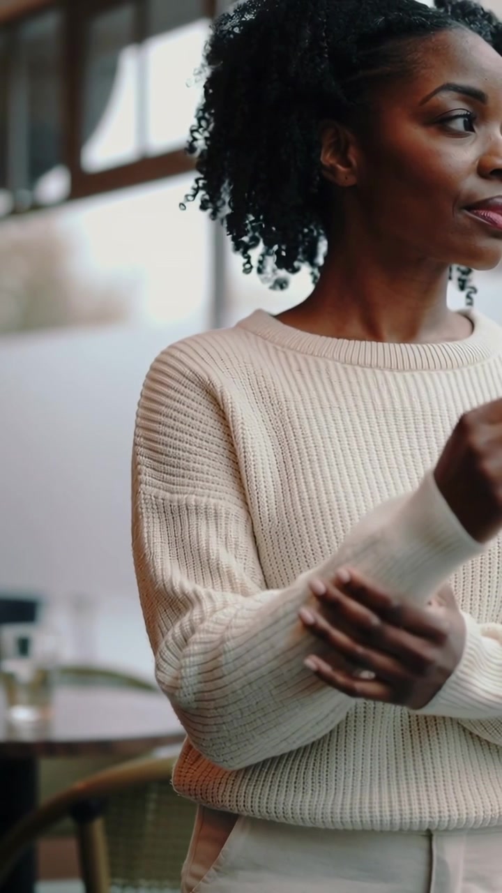 Vertical video: Smoothing woman adjusting cream sweater sleeves after hand rests by cafe window