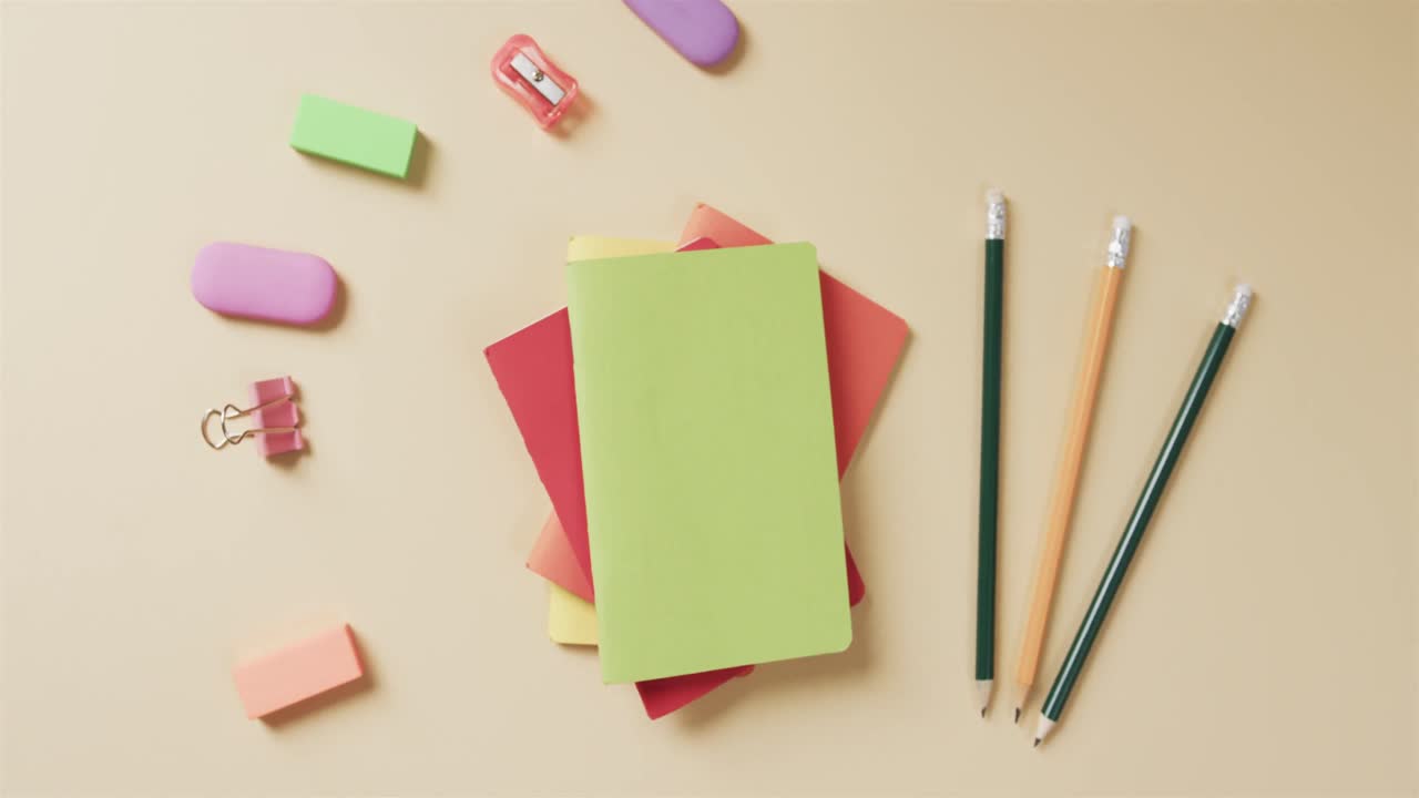 Overhead view of colourful notebooks with school stationery on beige background, in slow motion