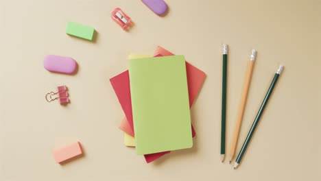 overhead view of colourful notebooks with school stationery on beige background, in slow motion