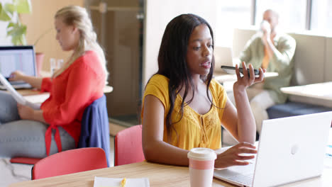 African-american-casual-businesswoman-talking-on-smartphone,-using-laptop-in-office,-slow-motion